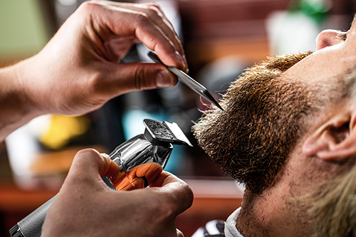 Barber works with a beard clipper. Hipster client getting haircut. Hands of a hairdresser with a beard clipper, closeup