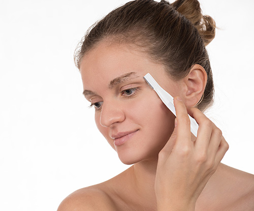 Young girl in a red towel caring for your eyebrows with trimmer