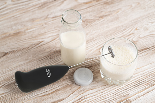 Handheld drink mixer. Black milk frother and milk in bottle and glass on wooden table